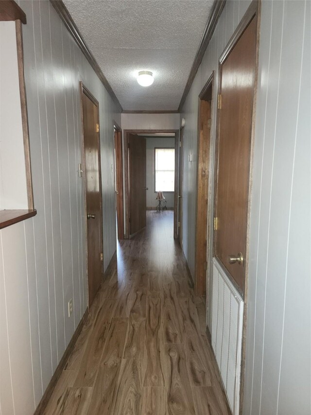 hallway with dark wood-type flooring, a textured ceiling, and ornamental molding