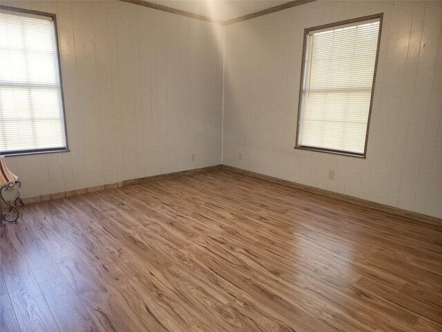 spare room with crown molding, wooden walls, and light wood-type flooring