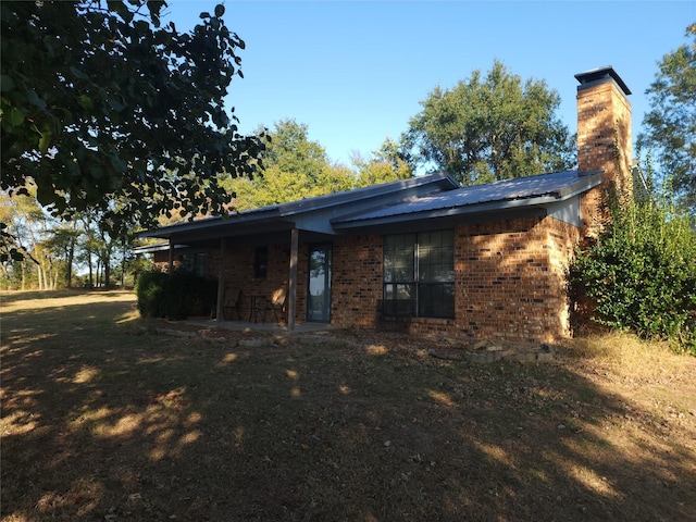 rear view of property with a yard, a chimney, and brick siding