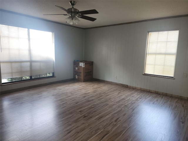 empty room featuring a wealth of natural light, crown molding, and wood finished floors