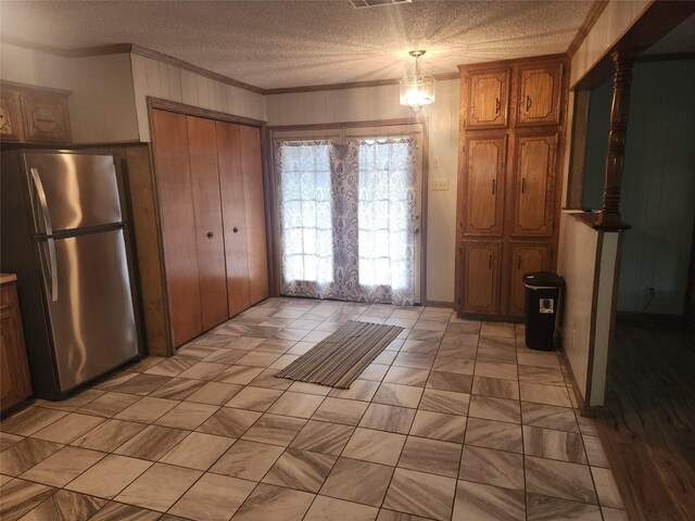 kitchen featuring pendant lighting, ornamental molding, a textured ceiling, a notable chandelier, and stainless steel refrigerator