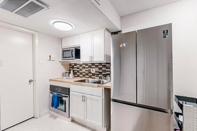 kitchen featuring wood counters, sink, decorative backsplash, appliances with stainless steel finishes, and white cabinetry