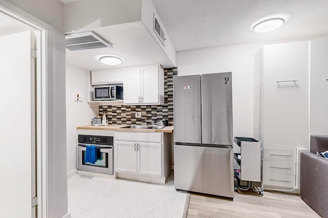 kitchen with white cabinets, sink, decorative backsplash, light wood-type flooring, and stainless steel appliances