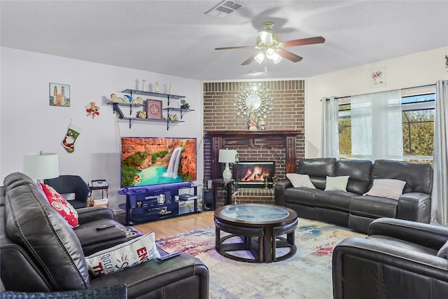 living room with a textured ceiling, wood-type flooring, ceiling fan, and a brick fireplace