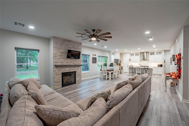 living room with ceiling fan, light hardwood / wood-style flooring, and a stone fireplace