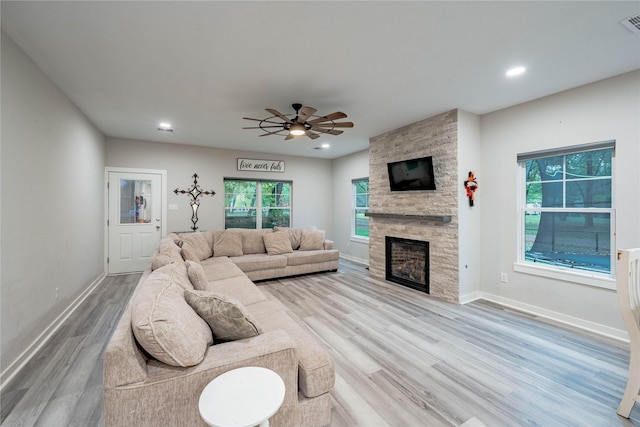 living room with a stone fireplace, light hardwood / wood-style flooring, and ceiling fan