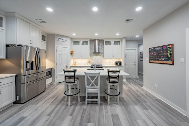 kitchen featuring sink, a center island with sink, wall chimney range hood, stainless steel appliances, and white cabinets