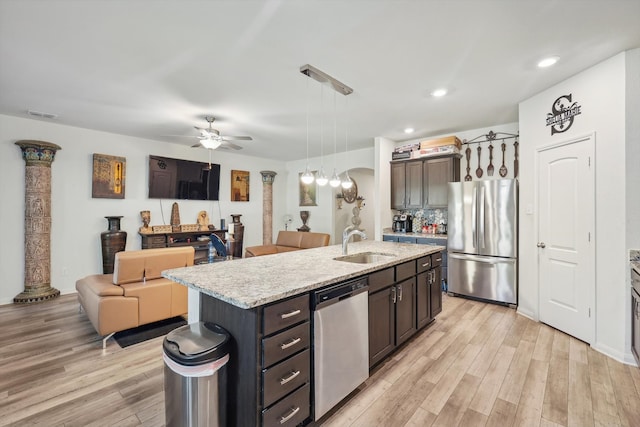 kitchen featuring a center island with sink, appliances with stainless steel finishes, decorative light fixtures, sink, and light hardwood / wood-style flooring