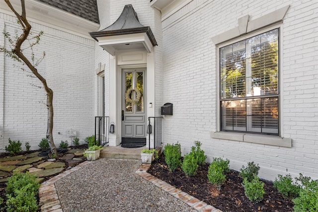 doorway to property with a shingled roof and brick siding