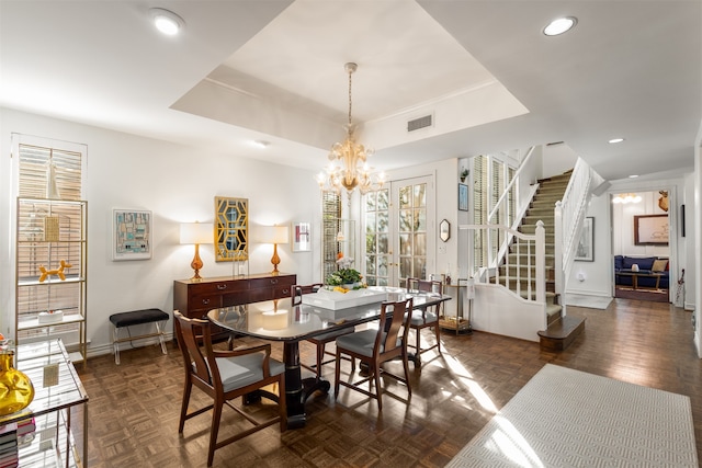 dining area featuring dark parquet flooring, a raised ceiling, and a chandelier