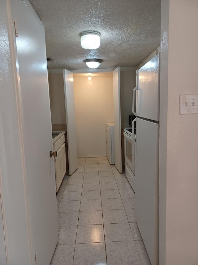 kitchen with light tile patterned floors, white appliances, washer and dryer, a textured ceiling, and white cabinets