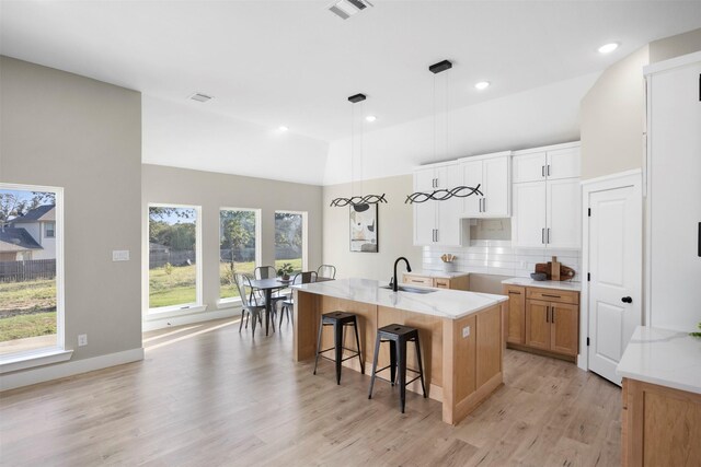 kitchen with white cabinets, sink, a kitchen island with sink, and backsplash