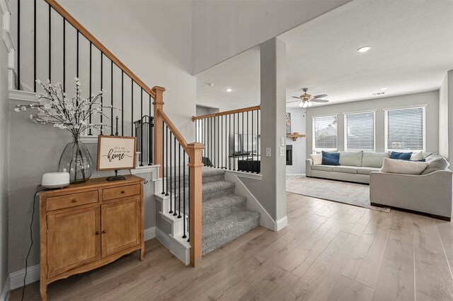 staircase with hardwood / wood-style floors, ceiling fan, and a fireplace