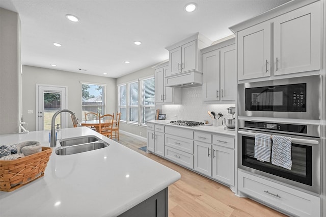 kitchen with sink, appliances with stainless steel finishes, backsplash, custom range hood, and light wood-type flooring