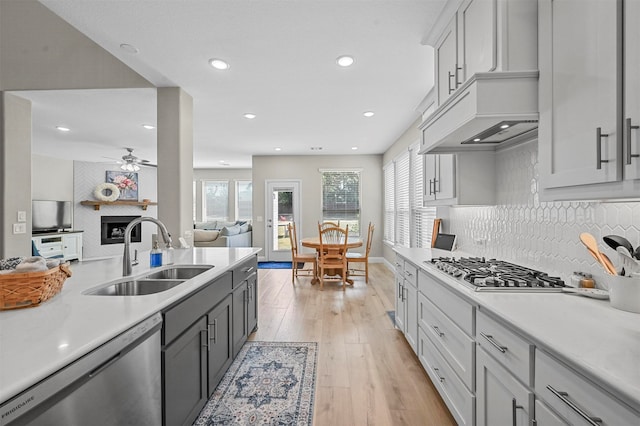 kitchen with light wood-type flooring, appliances with stainless steel finishes, decorative backsplash, sink, and ceiling fan