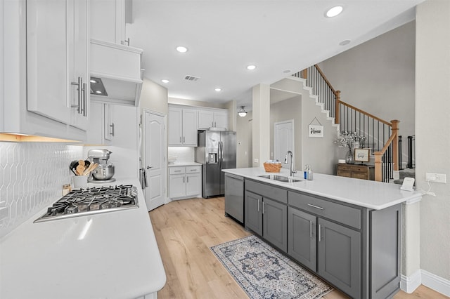 kitchen with gray cabinetry, light wood-type flooring, appliances with stainless steel finishes, and tasteful backsplash