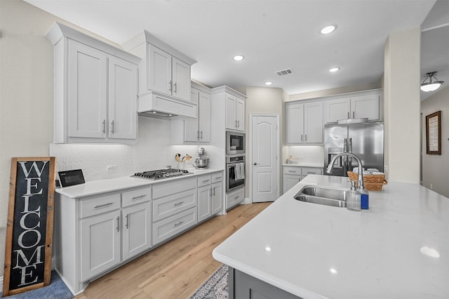 kitchen featuring sink, appliances with stainless steel finishes, custom exhaust hood, light wood-type flooring, and decorative backsplash