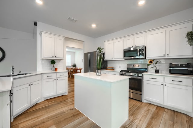 kitchen with light wood-type flooring, stainless steel appliances, sink, white cabinets, and a center island