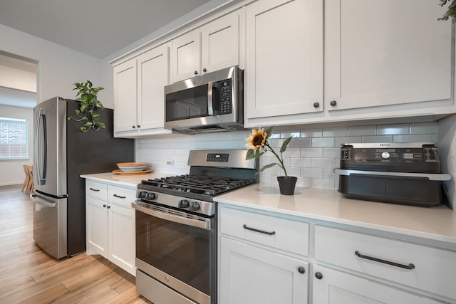 kitchen with white cabinets, appliances with stainless steel finishes, tasteful backsplash, and light hardwood / wood-style floors