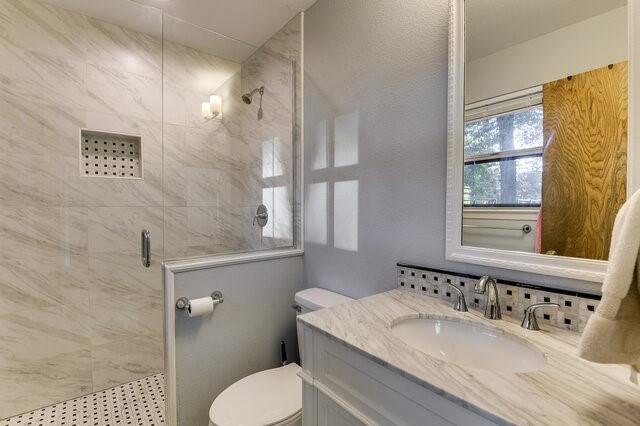 bathroom with a shower with shower door, vanity, and toilet