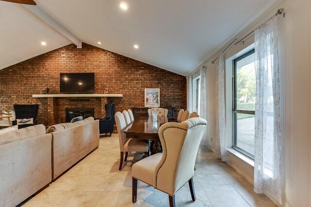 dining room with brick wall, vaulted ceiling with beams, and a fireplace