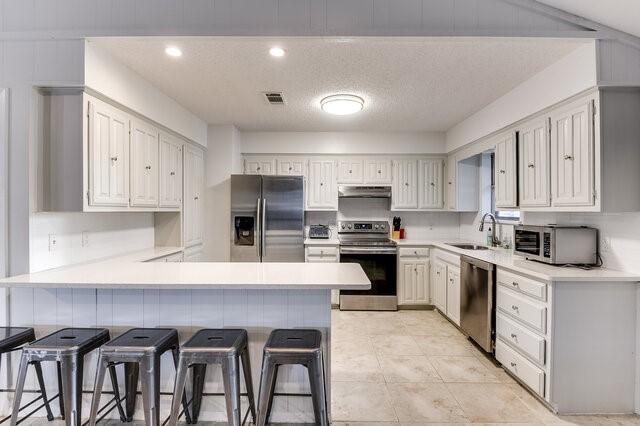 kitchen with white cabinetry, kitchen peninsula, appliances with stainless steel finishes, a kitchen breakfast bar, and sink