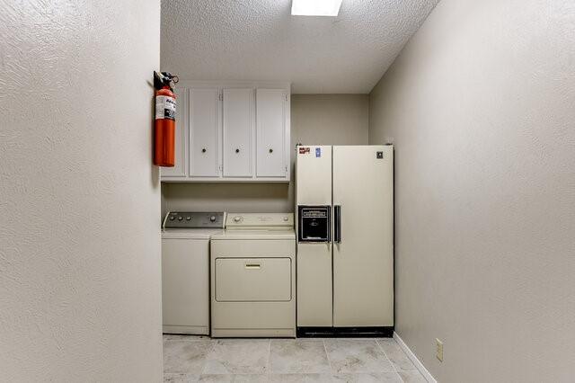 clothes washing area with washer and dryer, cabinets, and a textured ceiling