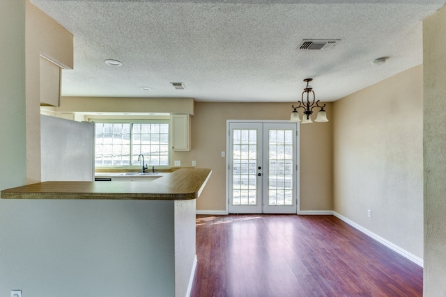 kitchen featuring pendant lighting, stainless steel fridge, wood-type flooring, french doors, and kitchen peninsula