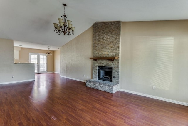 unfurnished living room with lofted ceiling, dark hardwood / wood-style floors, a brick fireplace, and a notable chandelier