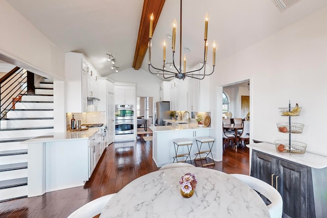 dining room with dark wood-type flooring, sink, a chandelier, high vaulted ceiling, and beam ceiling