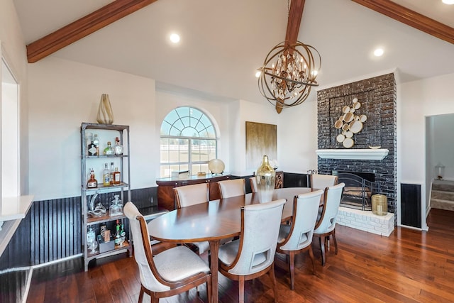 dining space featuring dark hardwood / wood-style flooring, a brick fireplace, lofted ceiling with beams, and a chandelier