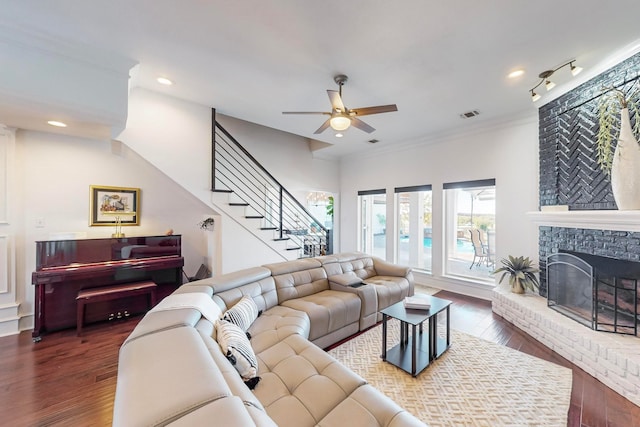 living room featuring ceiling fan, ornamental molding, dark hardwood / wood-style floors, and a brick fireplace