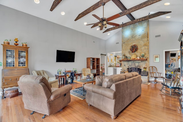 living room featuring light hardwood / wood-style floors, high vaulted ceiling, ceiling fan, beam ceiling, and a fireplace