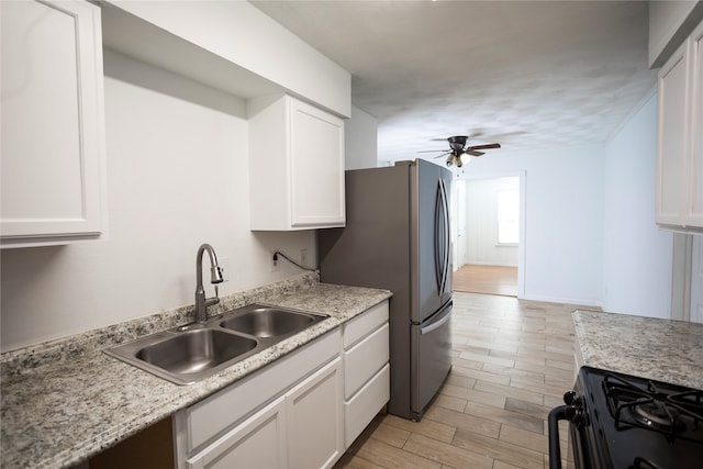 kitchen with light hardwood / wood-style floors, white cabinets, sink, stainless steel refrigerator, and black stove