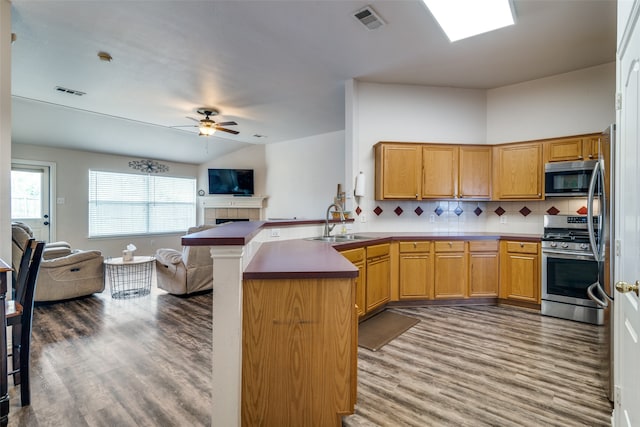 kitchen featuring stainless steel appliances, kitchen peninsula, decorative backsplash, hardwood / wood-style flooring, and sink