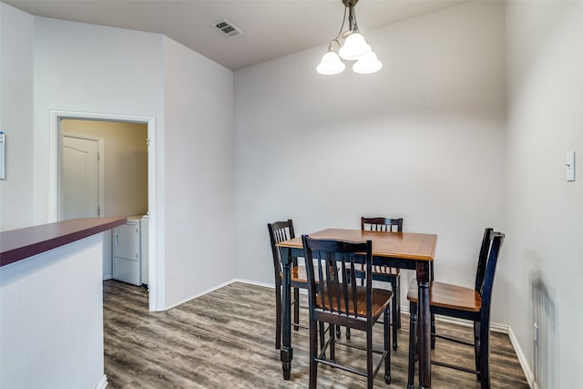 dining area featuring wood-type flooring, washer and dryer, and a notable chandelier