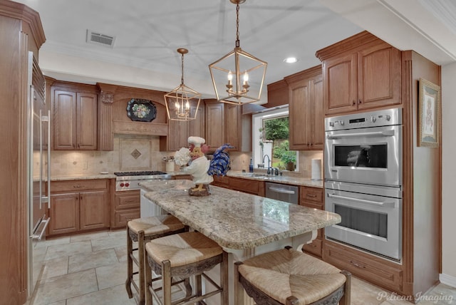 kitchen featuring stainless steel appliances, sink, light stone countertops, decorative light fixtures, and a center island