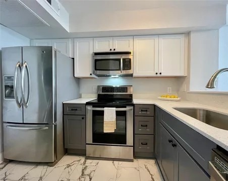 kitchen with white cabinetry, sink, light stone counters, and appliances with stainless steel finishes