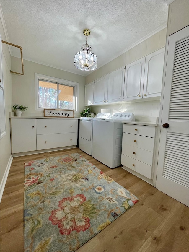 clothes washing area with washer and clothes dryer, cabinets, a textured ceiling, and light hardwood / wood-style flooring