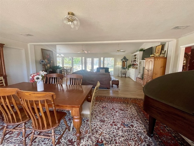 dining area featuring hardwood / wood-style floors, ceiling fan with notable chandelier, and a textured ceiling