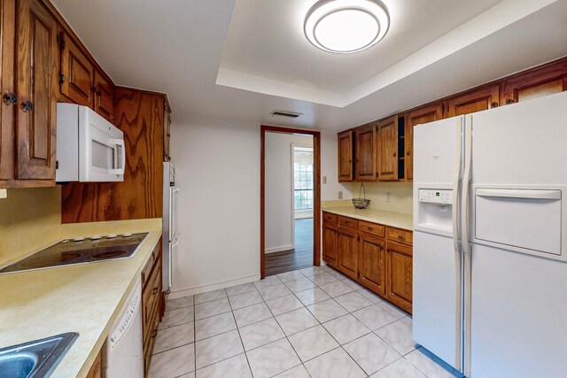 kitchen featuring light tile patterned floors, white appliances, a tray ceiling, and sink