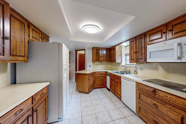 kitchen with a tray ceiling, white appliances, sink, and light tile patterned floors