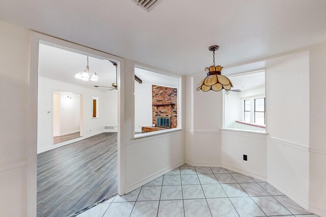 unfurnished dining area featuring light hardwood / wood-style flooring, lofted ceiling, ceiling fan, and a brick fireplace