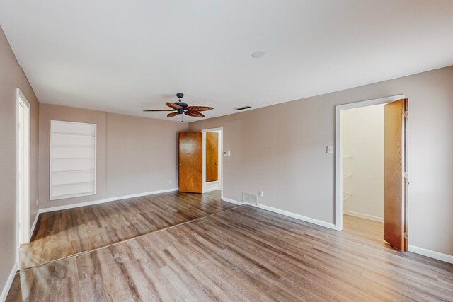 spare room featuring built in shelves, light wood-type flooring, and ceiling fan