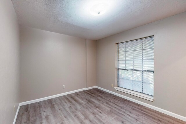 empty room with a textured ceiling and light hardwood / wood-style flooring