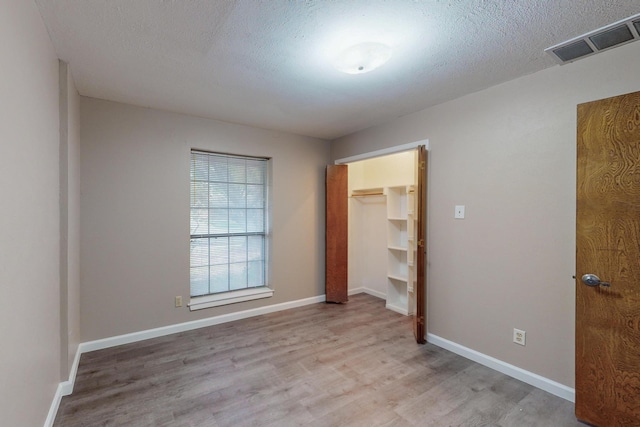 unfurnished bedroom with light wood-type flooring, a spacious closet, a textured ceiling, and a closet