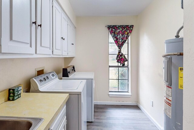 clothes washing area with hardwood / wood-style floors, water heater, cabinets, and washer and dryer