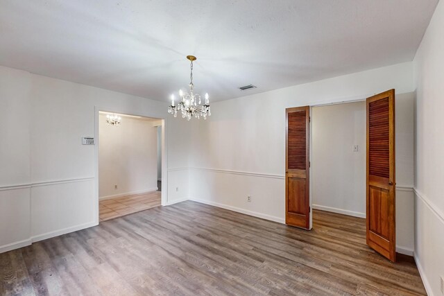 spare room with wood-type flooring and an inviting chandelier