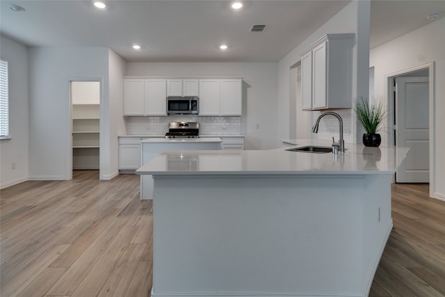 kitchen with white cabinets, sink, tasteful backsplash, light wood-type flooring, and appliances with stainless steel finishes