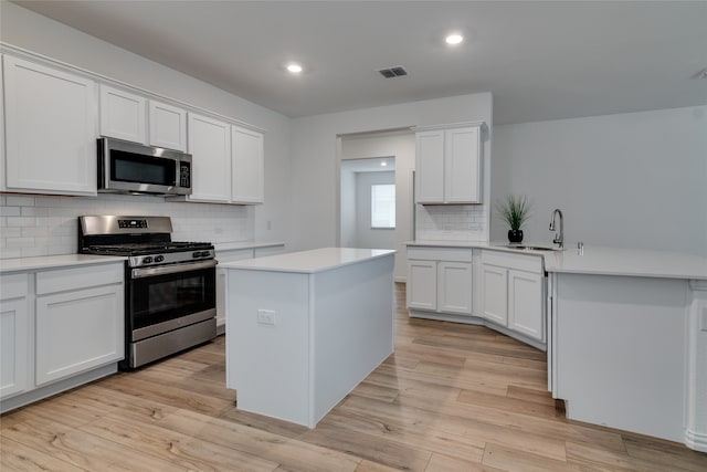 kitchen featuring sink, white cabinetry, stainless steel appliances, a center island, and light wood-type flooring